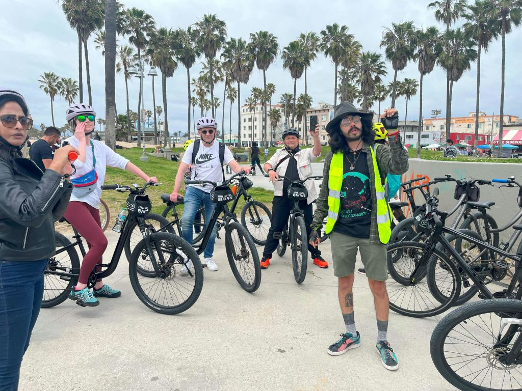 자전거를 타고 헬멧과 평상복을 착용한 채 야자수와 해변 산책로 근처에서 포즈를 취하는 사이클리스트 그룹.