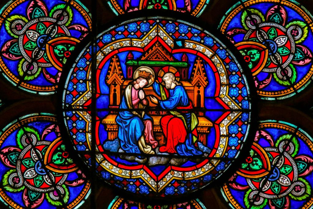 파란색과 빨간색 가운을 입은 두 개의 후광 형상이 화려한 배경으로 왕좌에 앉아 있는 스테인드글라스 창입니다.