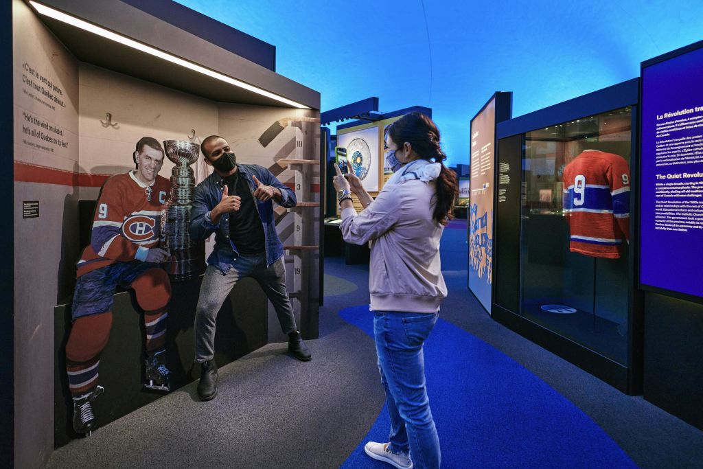 스마트폰으로 사진을 찍는 사람이 하키 선수 컷아웃과 스탠리컵 복제품 옆에서 포즈를 취하고 있습니다.