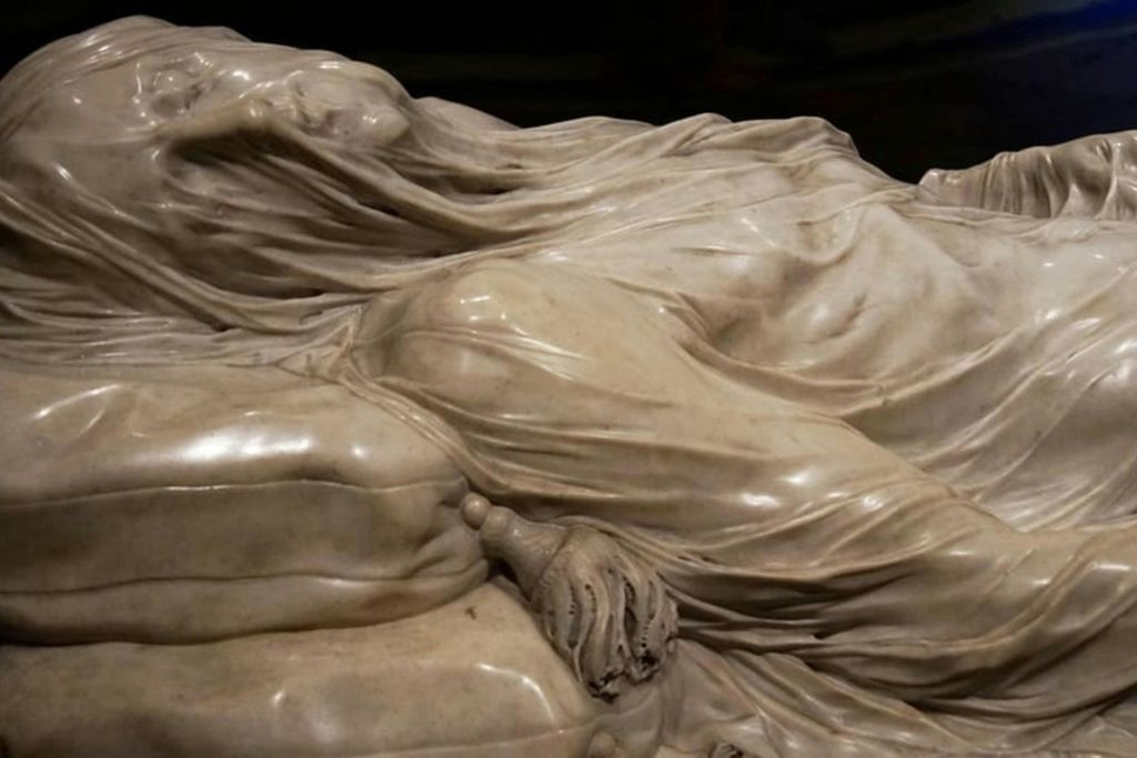 드레이핑된 천과 물건을 들고 있는 손의 복잡한 디테일을 묘사한 대리석 조각의 클로즈업.