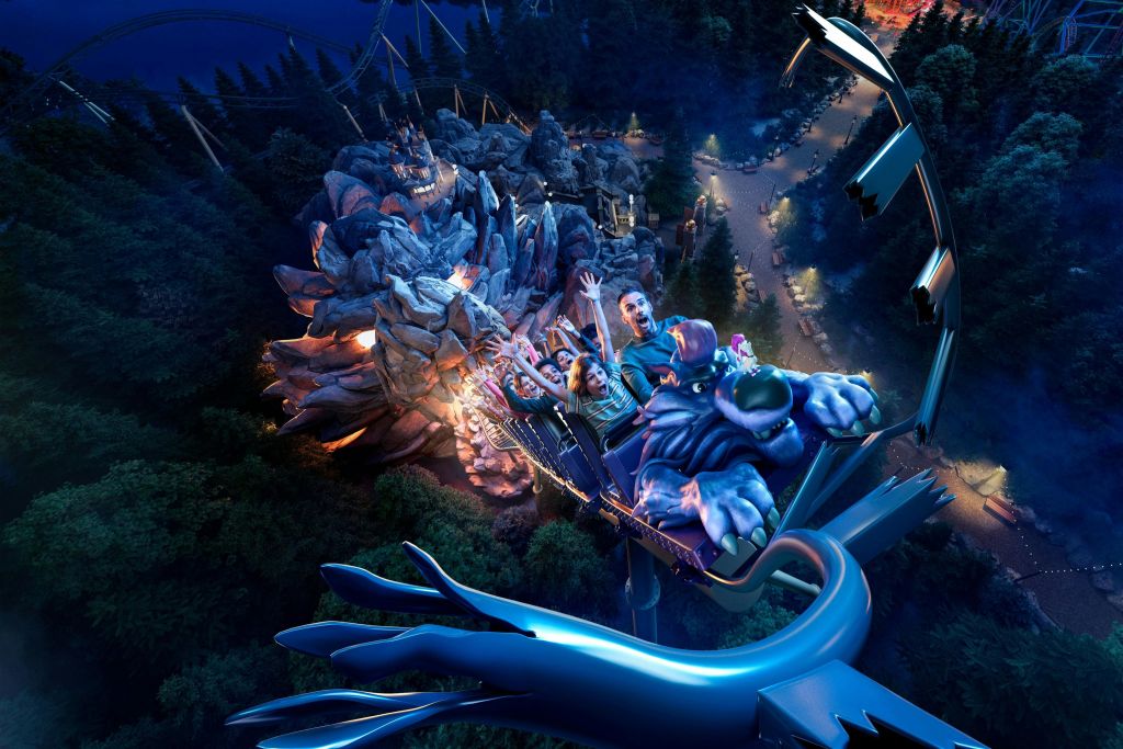 밤에 숲이 우거진 불빛이 비치는 놀이공원으로 둘러싸인 용을 테마로 한 롤러코스터를 타는 사람들.