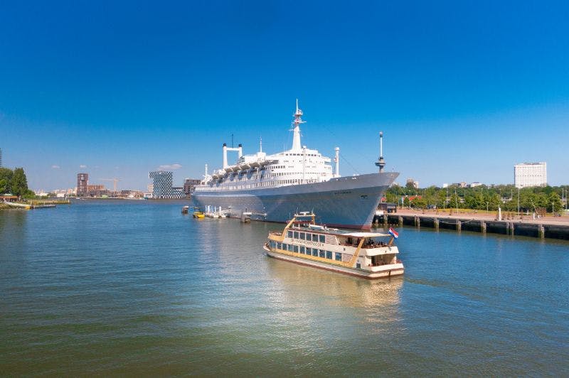 커다란 흰색 유람선이 부두에 정박했고, 근처에는 작은 보트가 맑고 푸른 하늘을 배경으로 항해하고 있습니다.