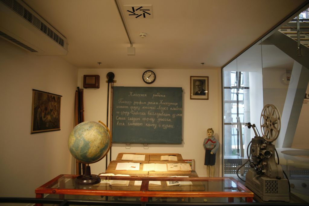 칠판이 있는 오래된 교실의 박물관 전시물, 책, 지구본, 마네킹, 빈티지 필름 프로젝터의 유리 진열장.