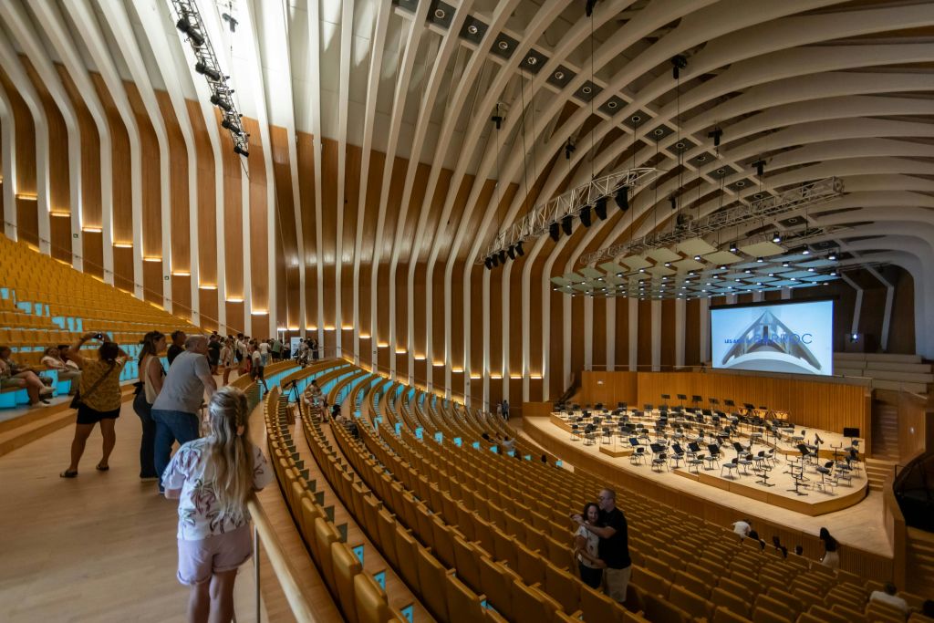 곡선형 목재 벽, 빈 노란색 좌석이 줄지어 있고 오케스트라 공연을 위해 마련된 무대가 있는 현대적인 콘서트 홀입니다.