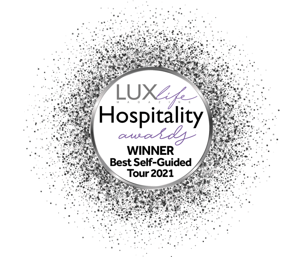 반짝이는 가장자리가 있는 원형 어워드 배지에는 "LUXlife Hospitality Awards. 2021년 최고의 셀프 가이드 투어에서 우승하세요. "