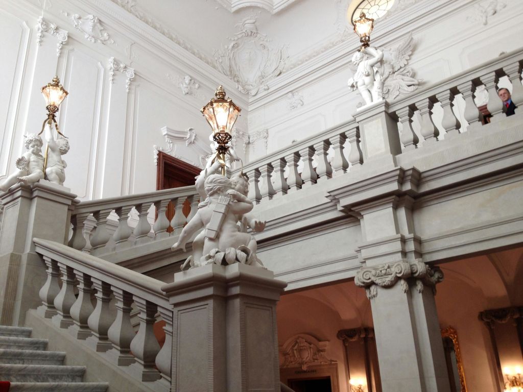 웅장하고 하얗고 정교하게 디자인된 내부 공간에 화려한 난간과 동상, 장식용 램프가 있는 우아한 계단.