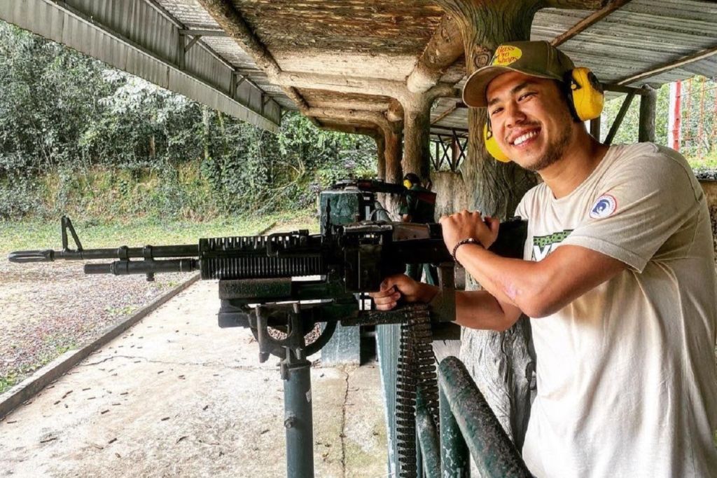 귀를 보호하는 웃는 남자가 실외 사격장에서 장착된 기관총을 작동합니다.