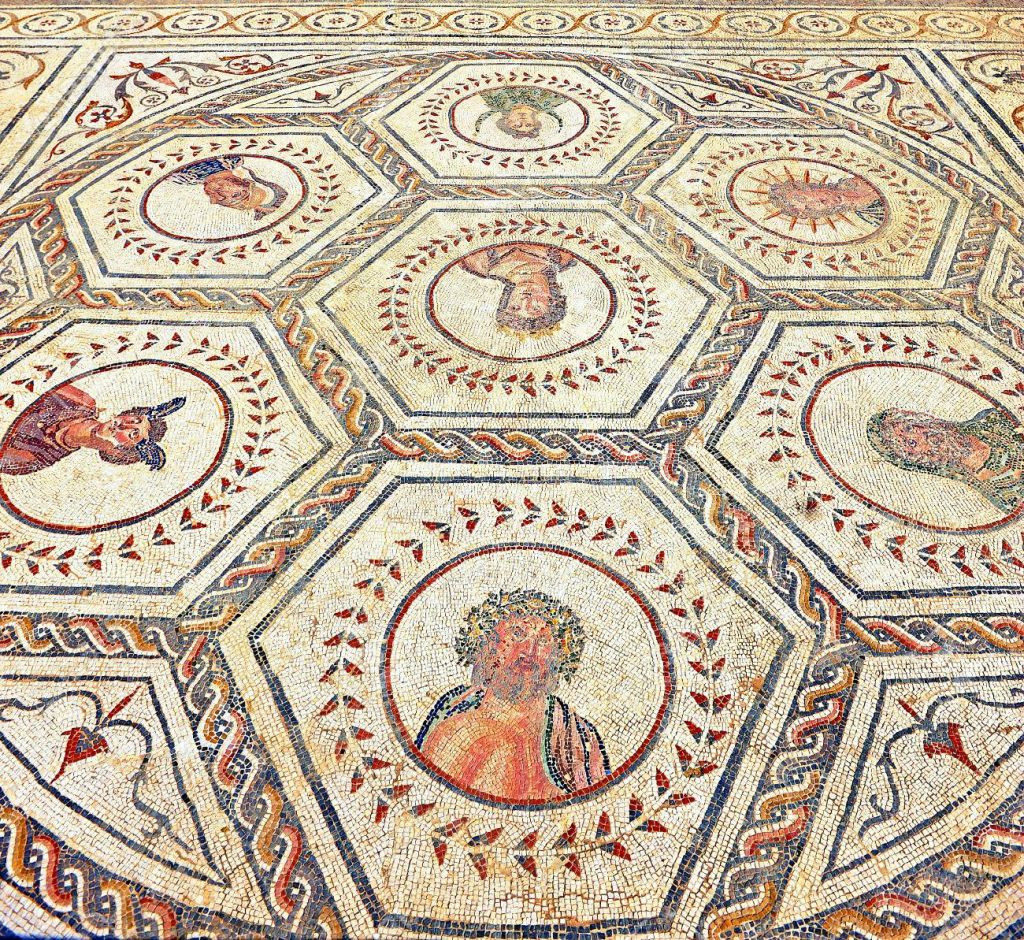 장식적인 테두리로 둘러싸인 다양한 인간과 동물의 모습을 묘사한 6각형 패턴의 복잡한 모자이크 바닥.