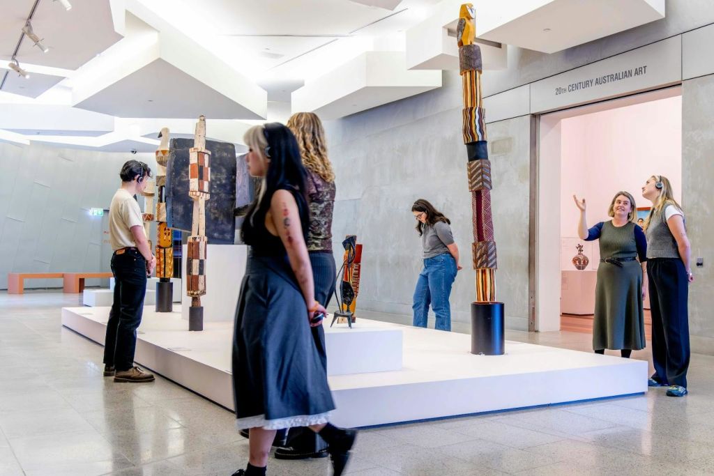 관람객들이 전시된 예술 작품을 감상하는 갤러리로, 받침대에 높이 솟은 조각 작품이 전시되어 있습니다. '20세기 호주 미술' 이라는 표지판이 있습니다.