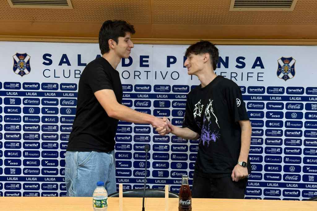 스폰서 로고와 'CLUB DEPORTIVO TENERIFE' 라는 문구가 적힌 기자회견장 앞에서 두 남자가 악수하고 있다.