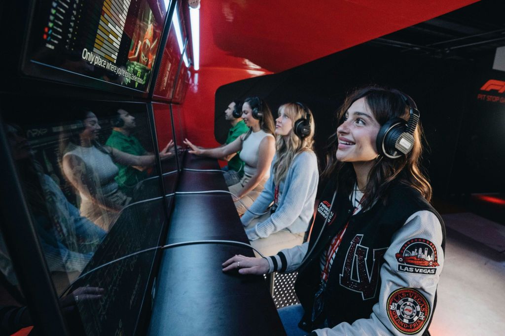 게임 또는 시뮬레이션 환경에서 헤드폰을 착용한 네 명이 일렬로 놓인 컴퓨터 화면에 앉아 있습니다.