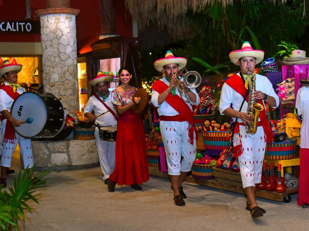 전통 복장을 한 뮤지션이 악기를 연주하고, 빨간 드레스를 입은 여성이 밤에는 화려한 시장 물품에 둘러싸여 미소를 짓습니다.