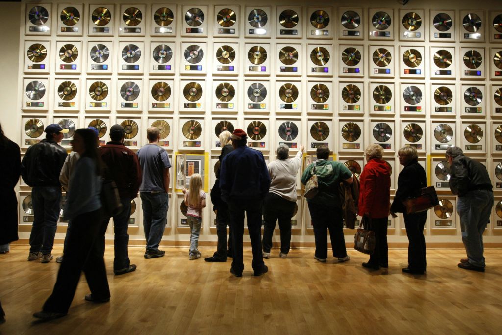 나무 바닥에 세워진 박물관이나 갤러리에서 금과 백금으로 장식된 커다란 벽을 구경하는 사람들.