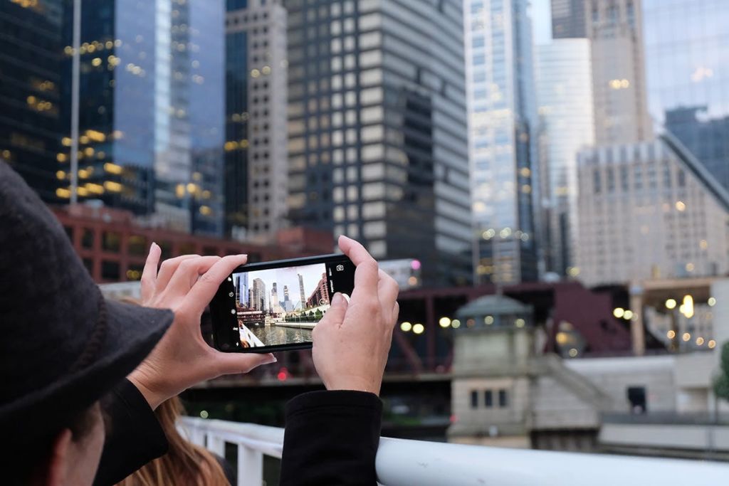 한 사람이 높은 건물과 다리를 배경으로 스마트폰으로 도시의 스카이라인을 촬영하고 있습니다.
