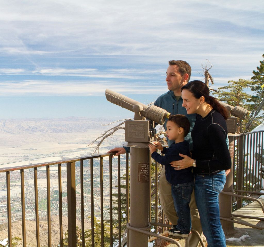 3인 가족이 쌍안경을 통해 산과 도시가 멀리 보이는 경치 좋은 전망을 감상합니다.