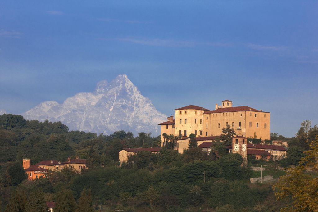 전경에 숲이 우거진 언덕과 맑은 하늘 아래 눈 덮인 산을 배경으로 한 역사적인 건물.