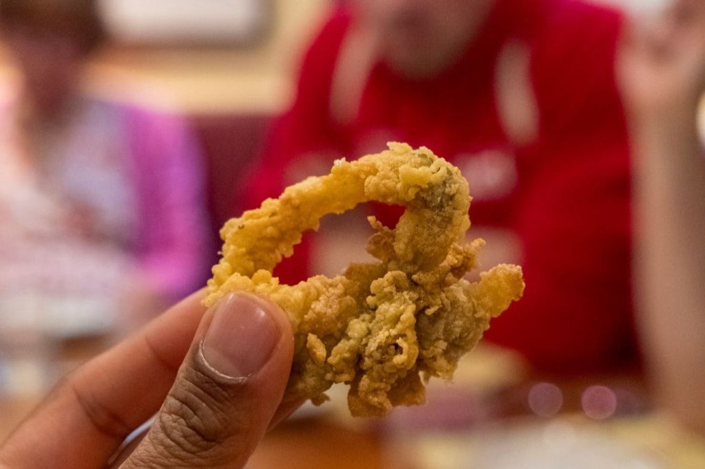 붉은 옷을 입은 사람이 흐릿한 배경에 튀긴 칼라마리 조각을 들고 있는 손.