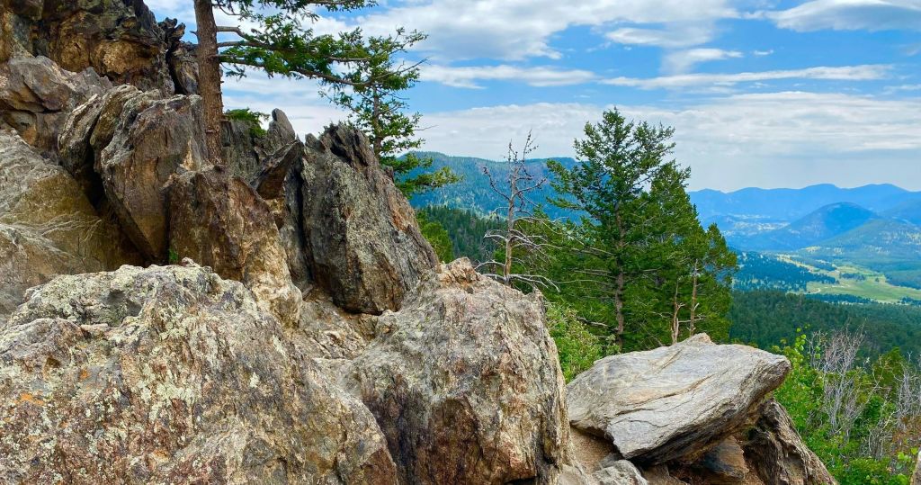 부분적으로 흐린 하늘 아래 숲이 우거진 산을 배경으로 원추형 나무로 둘러싸인 암반 수확.