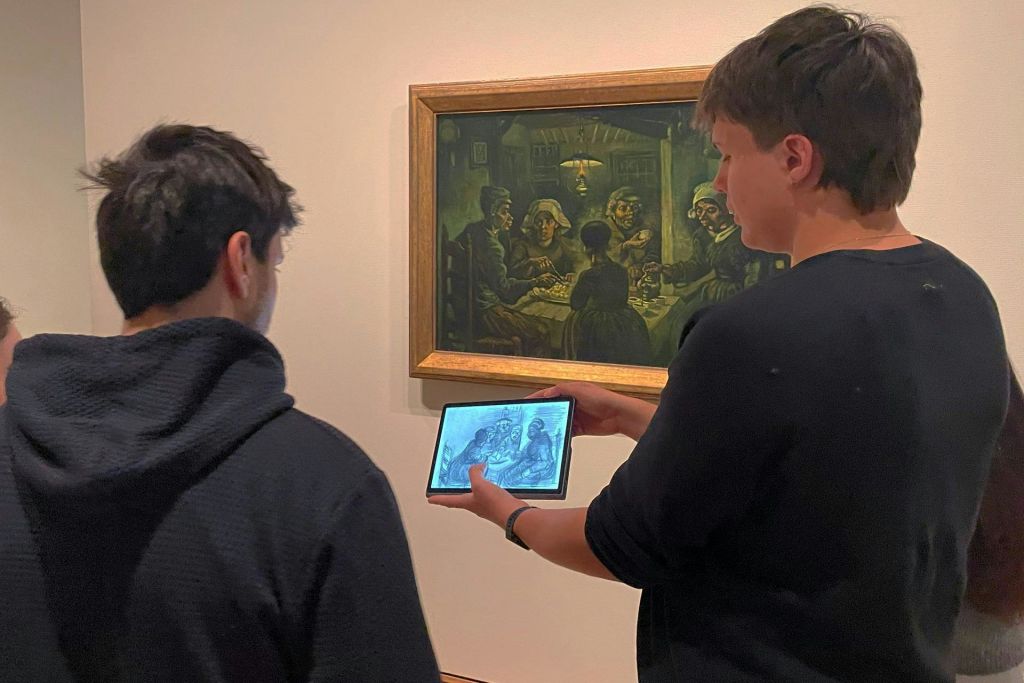박물관 벽에 있는 액자 그림 앞에 이미지를 표시하는 태블릿을 들고 있는 사람.