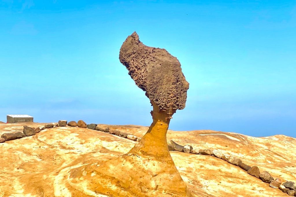 맑고 푸른 하늘을 배경으로 황량하고 모래가 많은 지형에 버섯 모양의 암석이 서 있습니다.