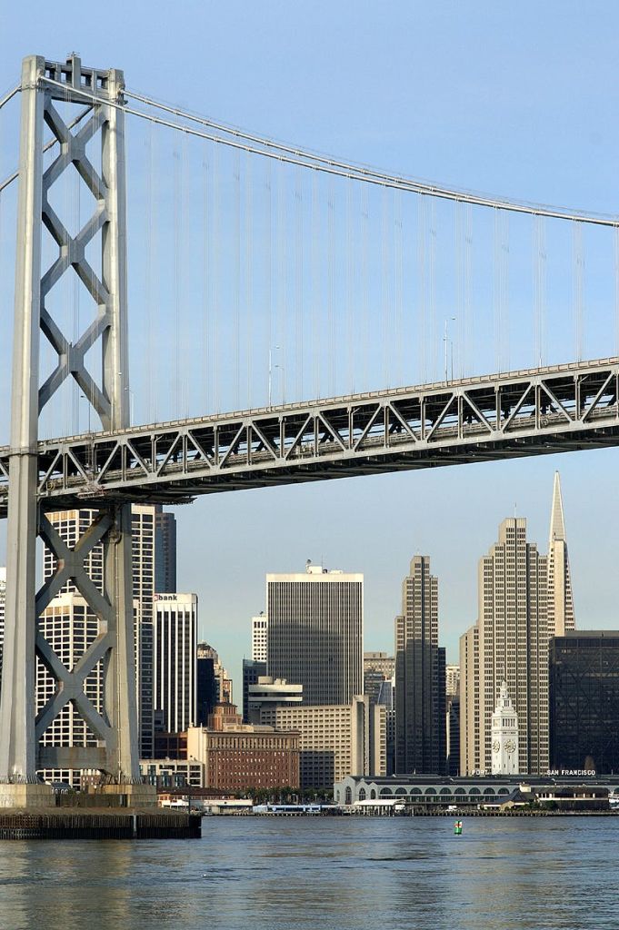 높은 건물과 뾰족한 고층 건물이 있는 도시의 스카이라인 위로 다리 구조물이 펼쳐져 있습니다.