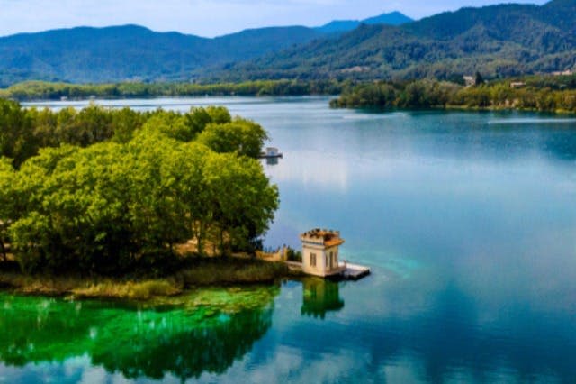 울창한 녹지와 먼 산으로 둘러싸인 맑고 고요한 호수가 있는 부두의 작고 노란 건물.