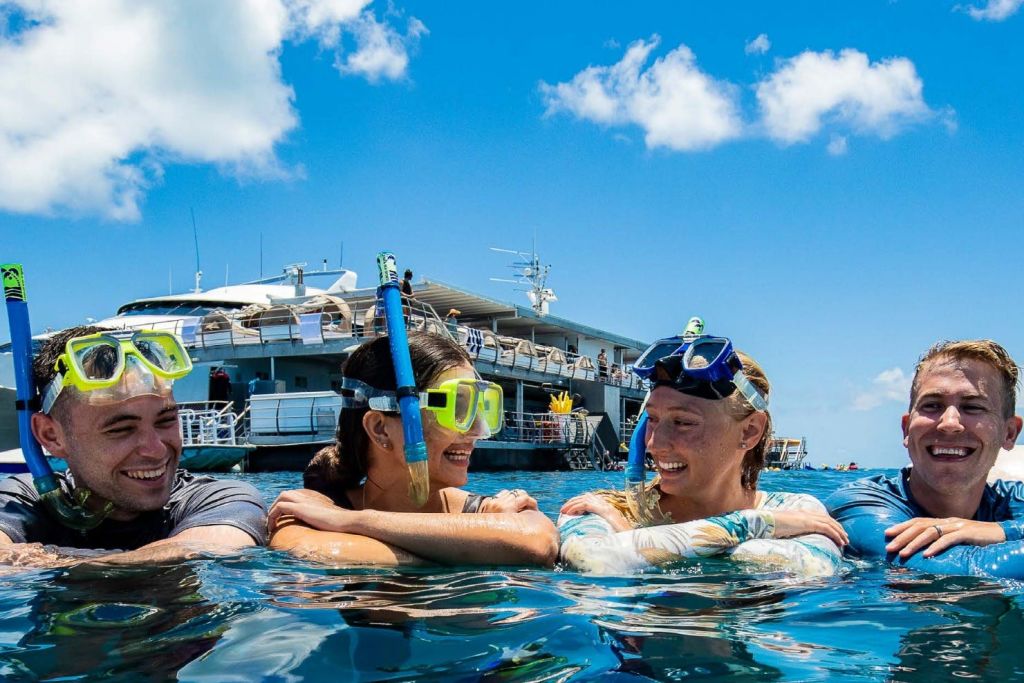 스노클링 장비를 착용한 세 사람이 밝고 푸른 하늘 아래 보트 근처 바다에서 미소를 짓고 휴식을 취하고 있습니다.