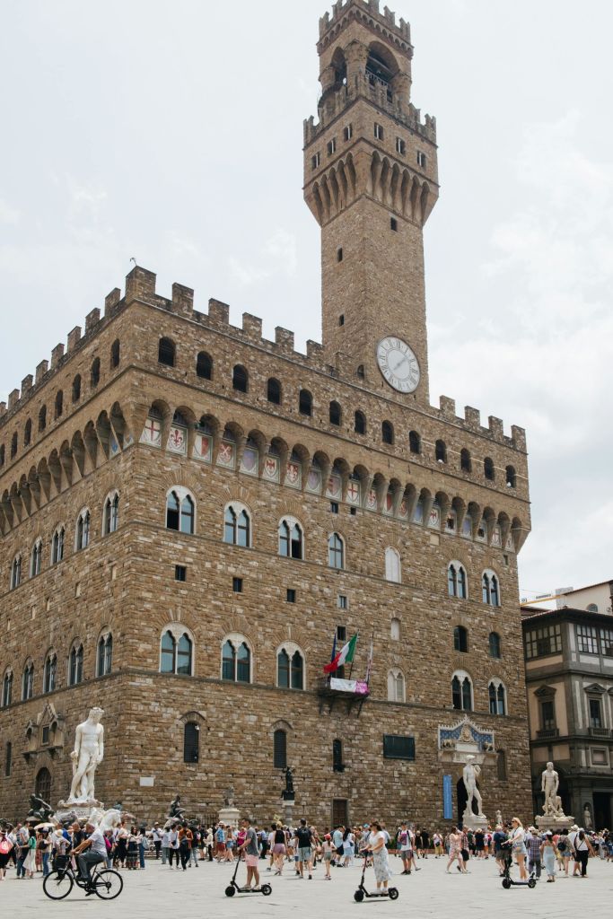 아치형 창문, 시계탑, 앞에 동상이 있는 크고 유서 깊은 석조 건물입니다. 이탈리아 국기가 발코니에 걸려 있습니다.