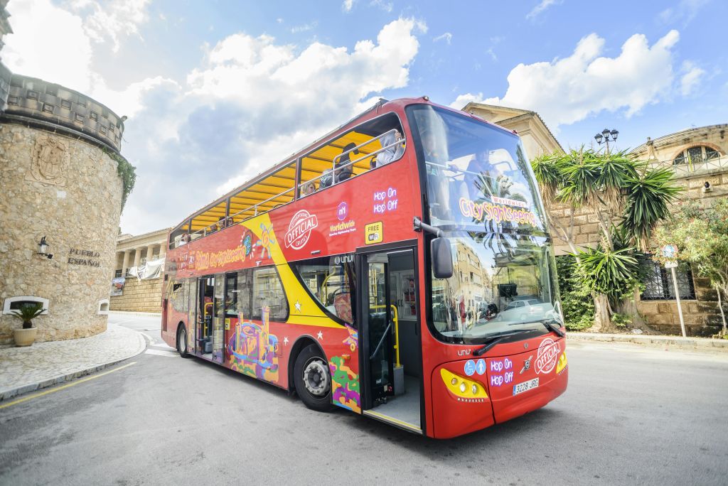 햇살이 내리쬐는 거리에는 탁 트인 상단이 있는 빨간색 2층 관광 버스가 주차되어 있습니다.