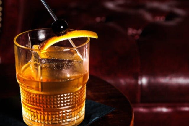 어두운 배경의 테이블 위에 오렌지 슬라이스와 칵테일 스틱 위에 체리를 장식한 아이스 큐브가 담긴 위스키 한 잔.