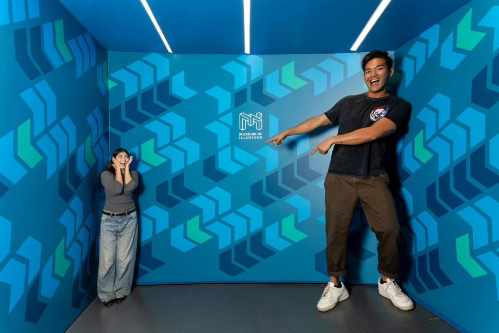 기하학적 무늬가 있는 방에 두 사람이 있고 벽에 '환상의 박물관' 이라는 글자가 있습니다. 하나는 훨씬 더 크게 보입니다.