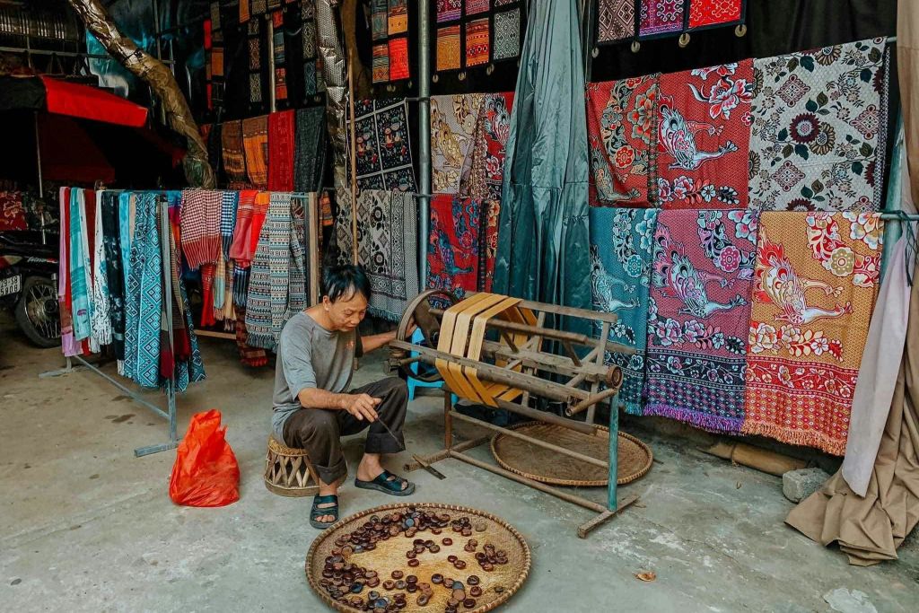 형형색색의 직물 가판대 앞에 있는 밤 바구니 옆의 작은 의자에 한 노인이 앉아 있습니다.