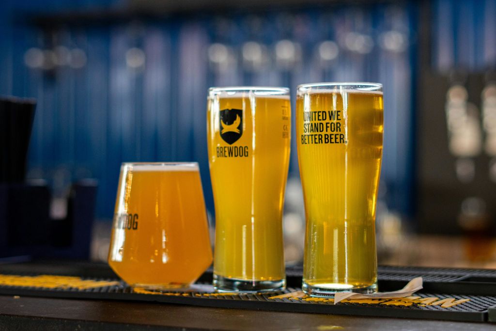 바 카운터에 맥주 3잔, 각각 BrewDog 브랜딩과 "UNITED WE STAND FOR BETTER BEER" 라는 추가 텍스트가 있습니다.