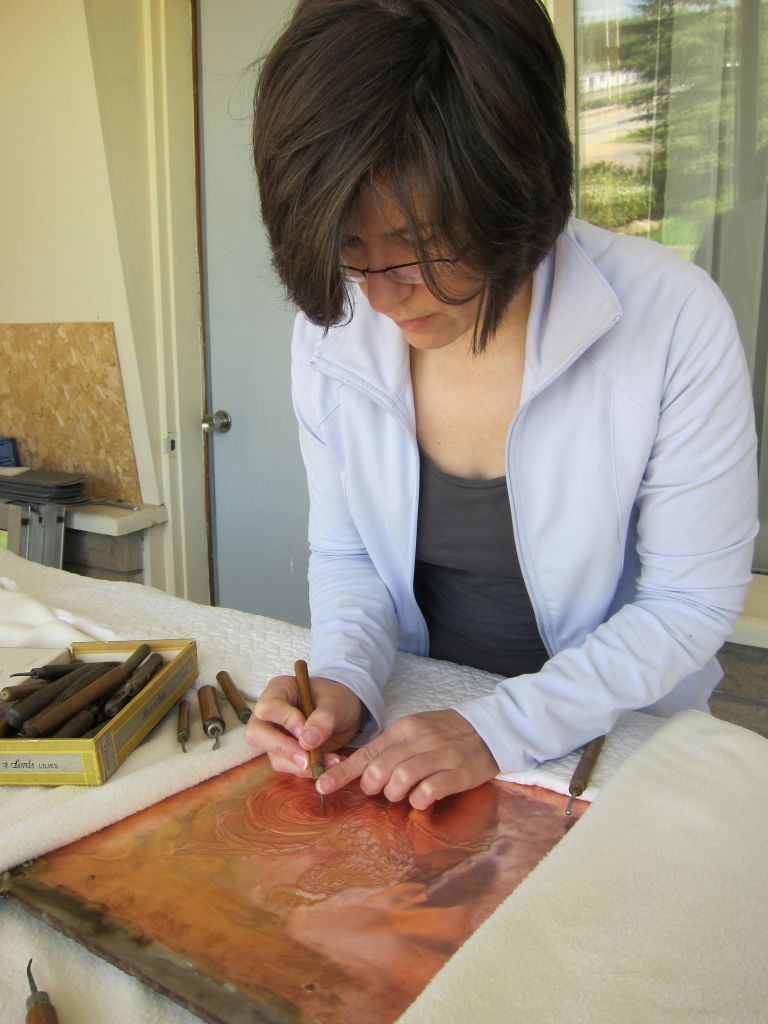 안경과 밝은 파란색 재킷을 입고 테이블에 그림을 그리거나 글을 쓰는 데 초점을 맞춘 짧은 머리카락을 가진 사람으로, 근처에 다양한 도구가 있습니다.