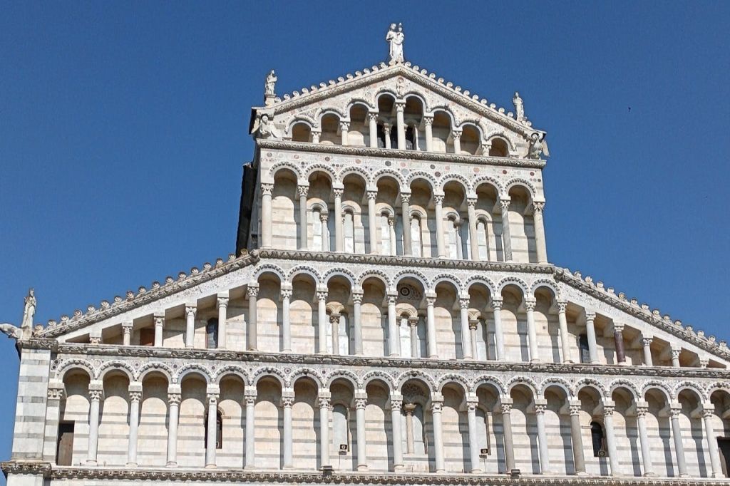 맑고 푸른 하늘을 배경으로 여러 줄의 아치와 조각상이 있는 웅장한 건물의 정면.