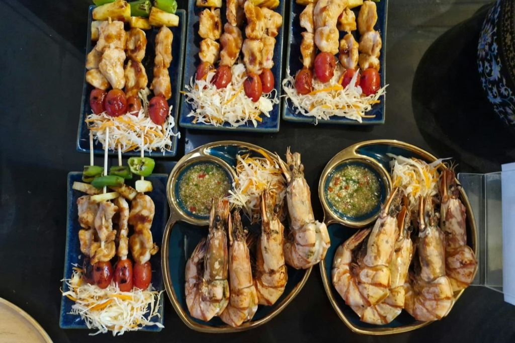 구운 새우와 야채 꼬치에 디핑 소스를 곁들인 접시는 잘게 썬 양배추 침대에서 제공됩니다.