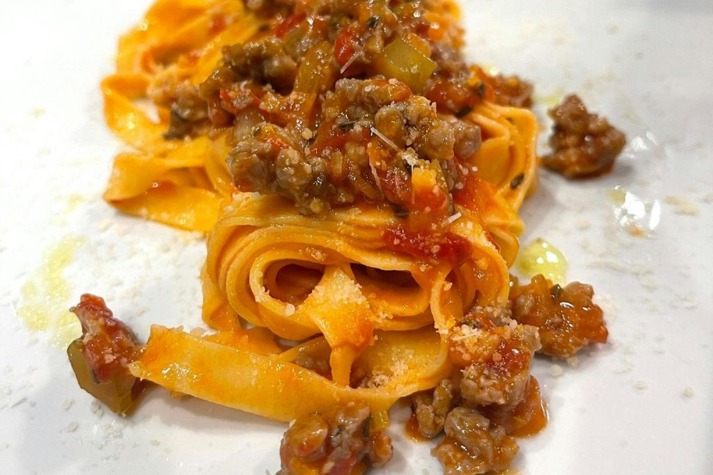 두툼한 고기와 토마토 소스를 토핑한 신선한 파스타에 갈은 치즈가 장식되어 있습니다.
