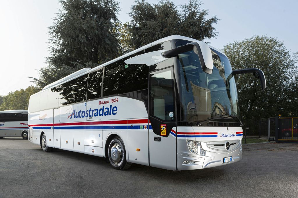 높은 나무를 배경으로 도로에 주차된 "Autostradale" 브랜딩이 있는 흰색 고급 코치 버스입니다.