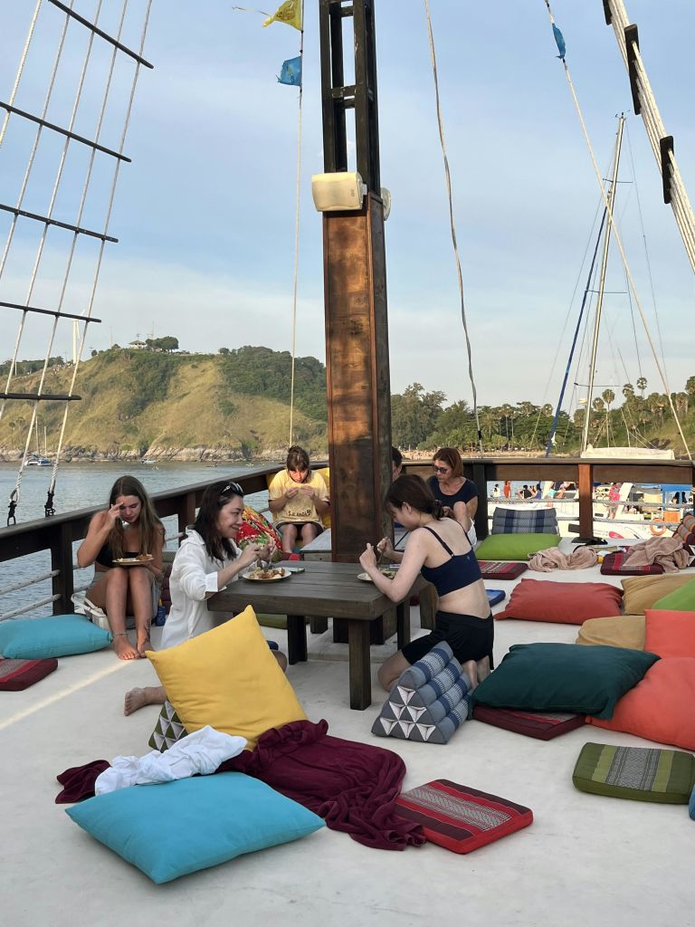 아름다운 해안선을 배경으로 보트를 타고 테이블 주변의 베개에서 식사를 하고 휴식을 취하는 사람들.