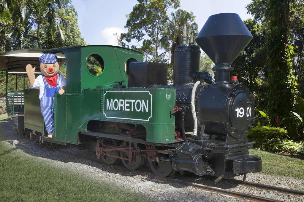 열차 엔지니어 의상을 입은 사람이 나무로 둘러싸인 '모레튼' 이라는 이름의 녹색 열차 엔진 위에 서 있습니다.