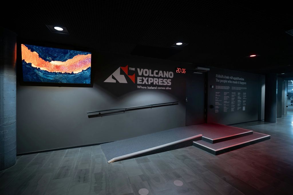 "The Volcano Express" 브랜딩, 램프, 계단, 디지털 디스플레이가 있는 현대적인 전시 공간의 내부.