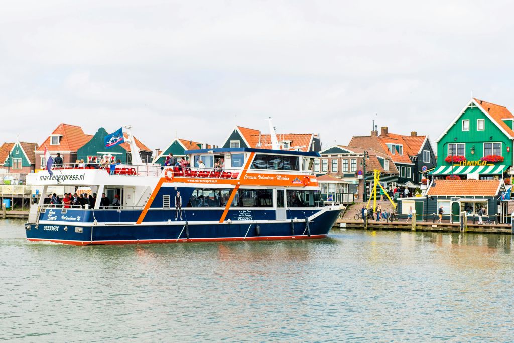 유럽 전통 건물이 있는 해안 근처에 2층 크루즈 보트가 정박해 있습니다.