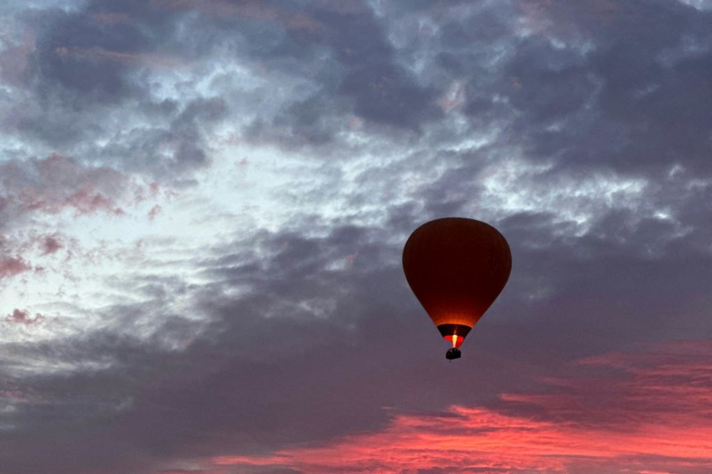 노을이 질 무렵 활기차고 흐린 하늘을 배경으로 열기구가 실루엣으로 배치되어 있으며, 풍선 아래에는 빛나는 버너가 있습니다.