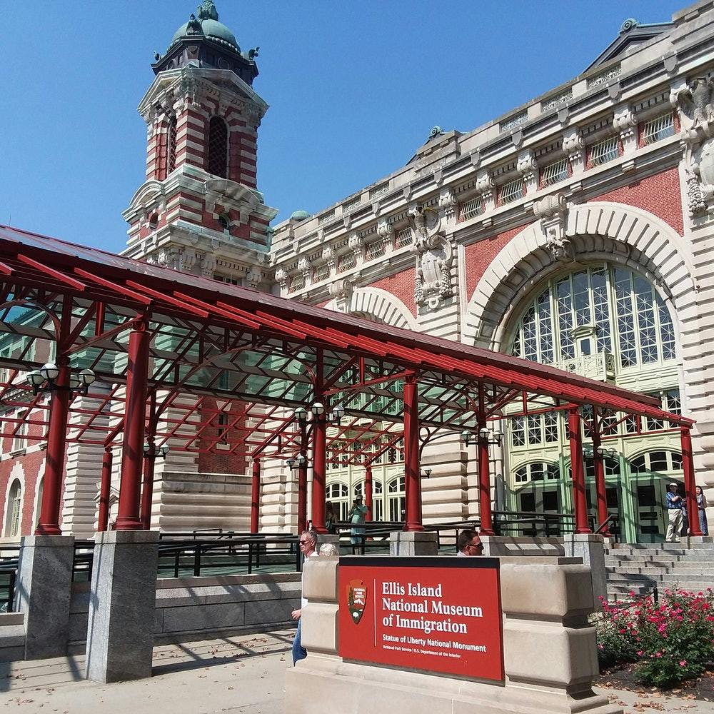 엘리스 섬 국립 이민 박물관은 붉은 벽돌 외관, 커다란 아치형 창문, 출입구 표지판을 갖추고 있습니다.