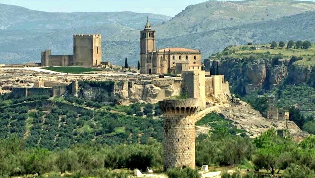 험준한 언덕 꼭대기에는 청명한 하늘 아래 푸른 풍경과 먼 산으로 둘러싸인 유서 깊은 석조 성곽과 탑이 있습니다.