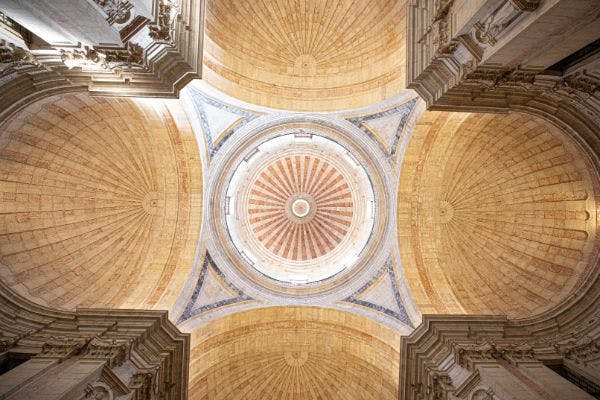 여러 개의 아치로 둘러싸인 정교한 조각과 따뜻한 색조의 동심원 패턴이 돋보이는 화려한 돔 천장.