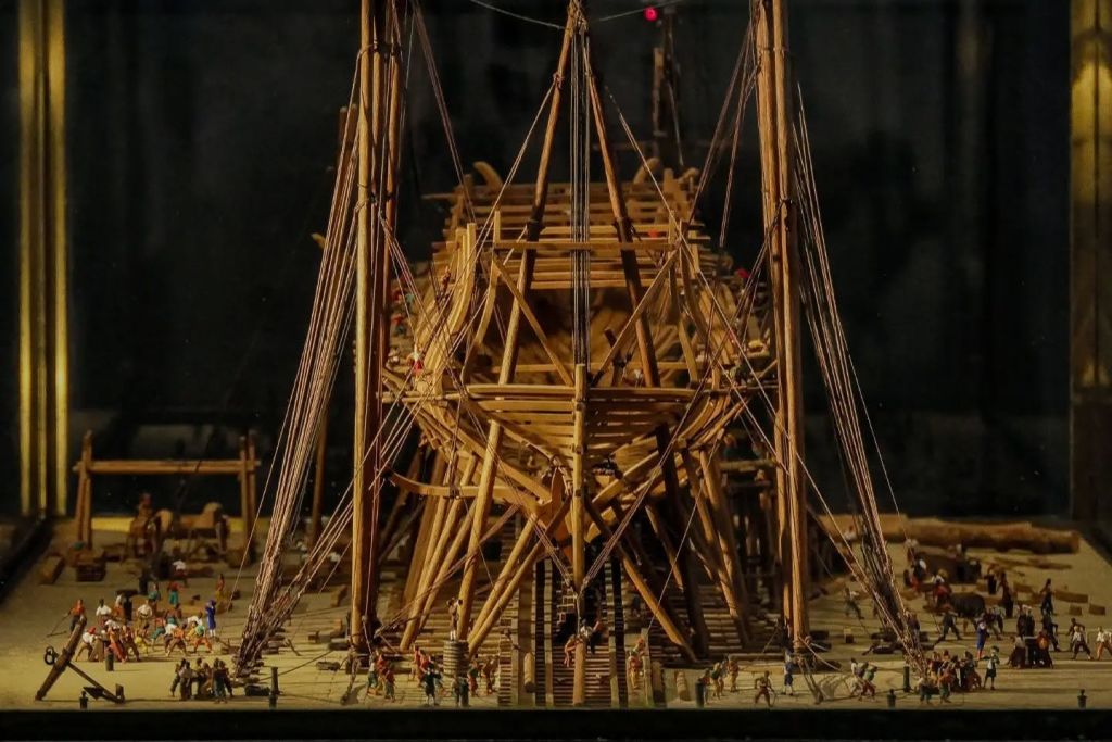 비계와 리깅으로 둘러싸인 미니어처 피규어가 주위를 둘러싸고 있는 상세한 목조 선박입니다.