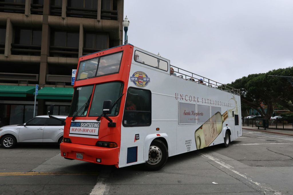 "Uncork Extraordinary" 와 와인병 광고가 있는 2층 관광 버스입니다. 상부 갑판에는 몇 명의 승객이 있습니다.