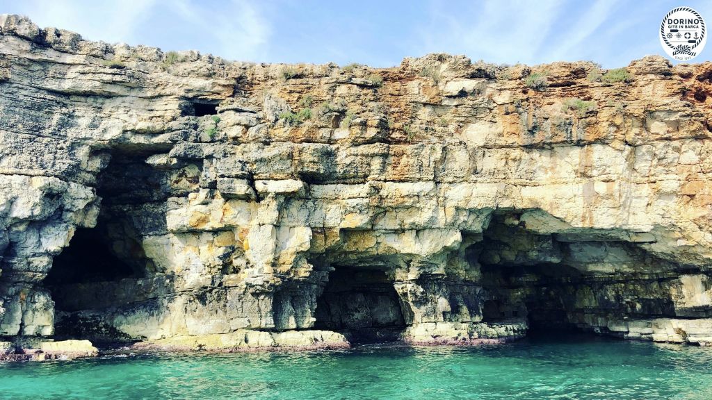 부분적으로 흐린 하늘 아래 청록색의 맑은 물과 경계를 이루는 바닷물 가장자리에 커다란 동굴이 있는 바위 절벽.