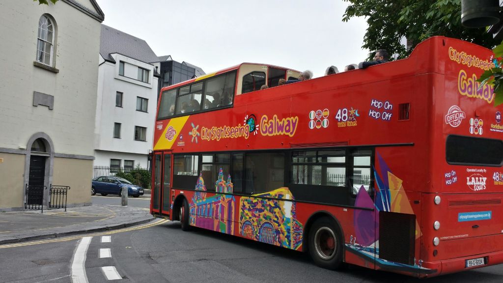 "골웨이 시내 관광" 표지판이 있는 빨간색 2층 버스와 상부 갑판에 있는 승객들은 거리를 지나갑니다.